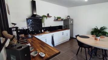 A modern kitchen with white cabinets, a black stove, and a stainless steel refrigerator. There is a dining table with chairs and a potted plant on the table.