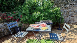 An outdoor patio with a table set for a meal, surrounded by greenery and a stone wall.