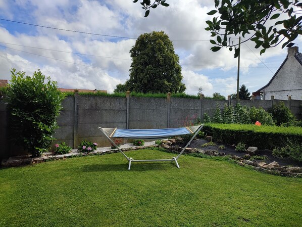 A hammock in a grassy backyard with a stone wall and a tree.