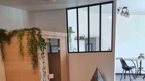 A modern interior with a tiled floor, a wooden partition with greenery, a small table with a decorative item, wicker chairs, and a white birdcage.