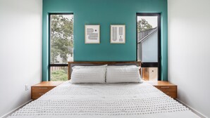 Een slaapkamer met een blauwgroene wand, een houten bedframe, witte beddengoed en twee ingelijste kunstwerken boven het bed.