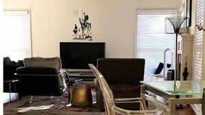 Ein Wohnzimmer mit einer Couch, einem Fernseher, einem Glastisch und einem Teppich.
