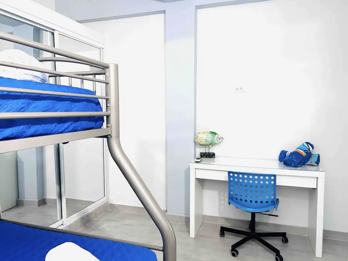Una cama litera con colchón azul, un escritorio con un globo y una silla azul, y una mochila azul sobre el escritorio.