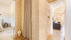 A room with a tiled floor, a striped curtain, and a sofa in the background. - 3632 Trullo Alcova del Dodo by Perle di Puglia (Ostuni)