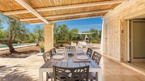 An outdoor dining area with a wooden table set for four, surrounded by chairs, under a bamboo pergola. - 3632 Trullo Alcova del Dodo by Perle di Puglia (Ostuni)
