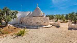 A stone structure with a conical roof, surrounded by a gravel area and sparse vegetation. - 3632 Trullo Alcova del Dodo by Perle di Puglia (Ostuni)
