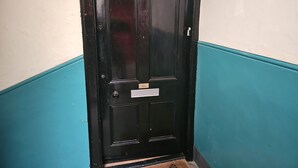A black door with a nameplate, set in a corner with teal and white walls. - Snug - Abhainn Apartment (Helensburgh)