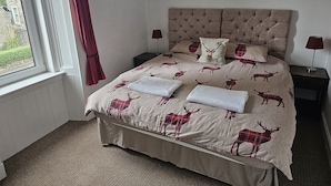 A bedroom with a bed featuring a deer print bedspread, a tufted headboard, and two bedside lamps. - Snug - Abhainn Apartment (Helensburgh)