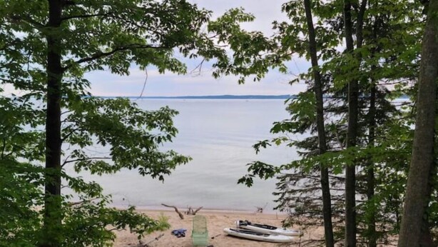 A beach with kayaks and a green chair, surrounded by trees. - West Bay House Private Frontage in Traverse City (Traverse City)