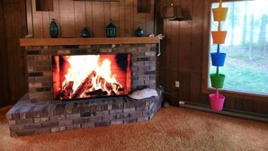 A fireplace with a fire, wooden panel walls, a painting above the mantel, and a window with a view of trees. - West Bay House Private Frontage in Traverse City (Traverse City)