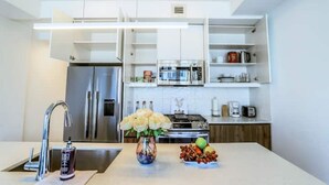 Een moderne keuken met een inbouwkoelkast, fornuis en magnetron. Op het aanrecht staat een vaas met bloemen en een schaal fruit.