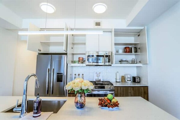 A modern kitchen with a built-in refrigerator, stove, and microwave. There is a vase with flowers on the counter and a bowl of fruit. - ✨ Stylish Walkout Condo in the Heart of Trendy Kensington ✨ (Calgary)