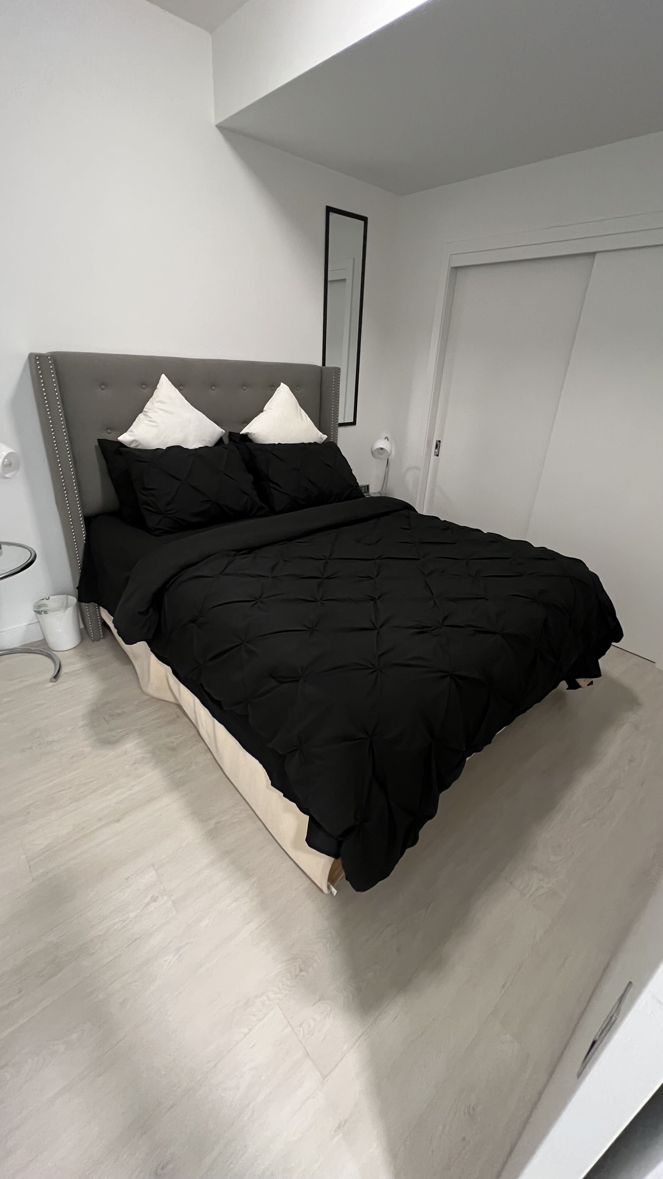 Un dormitorio moderno con un cabecero tapizado en gris, un edredón acolchado negro y dos almohadas blancas.