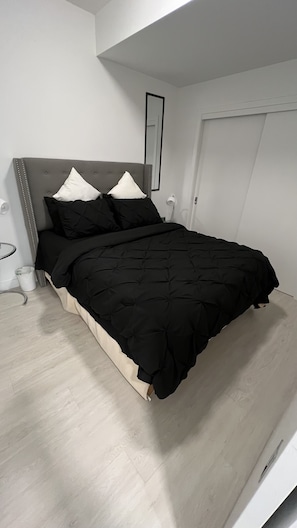 A modern bedroom with a grey upholstered headboard, a black quilted bedspread, and two white pillows.