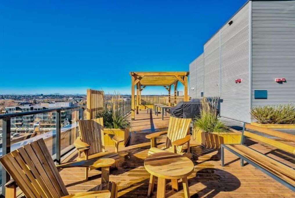 A rooftop terrace with wooden furniture, a pergola, and a view of the city.