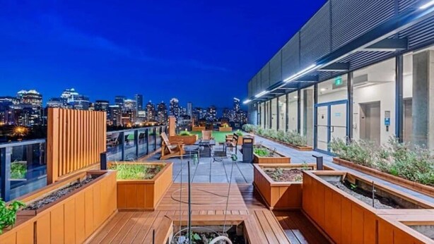 Een dakterras met houten plantenbakken, zitgedeeltes en een uitzicht op de skyline van de stad in de schemering.