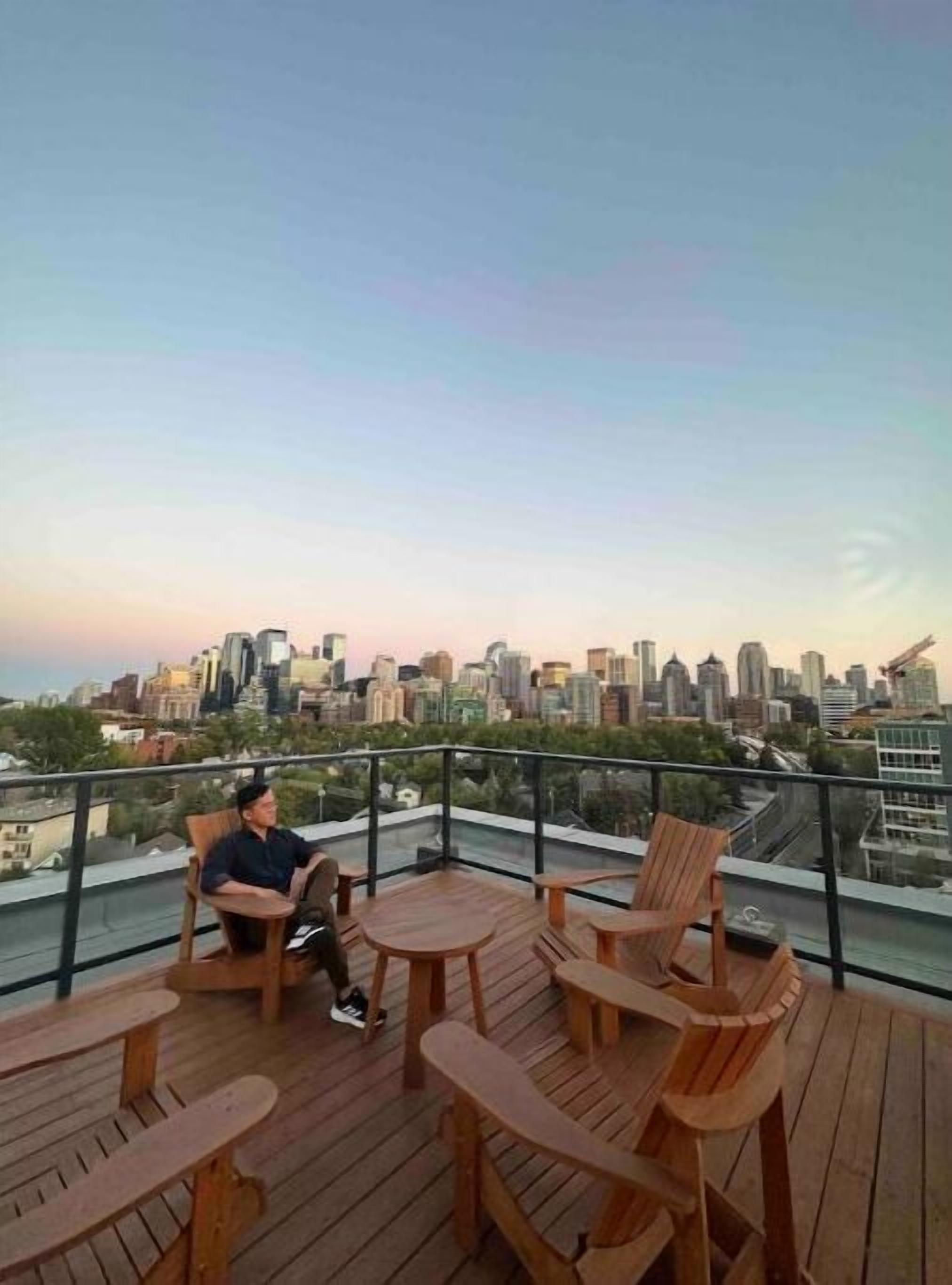 A rooftop terrace with wooden furniture and a city skyline view.