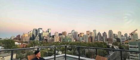 A rooftop terrace with wooden furniture and a city skyline view.