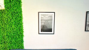 Un canapé bleu est placé contre un mur blanc, lequel est adjacent à un mur vert. Un tableau encadré représentant une jetée est accroché au mur.