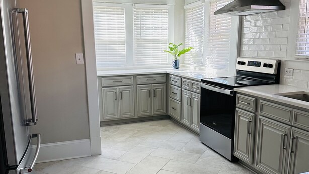 Una cocina moderna con armarios blancos, un refrigerador de acero inoxidable y una campana extractora negra.