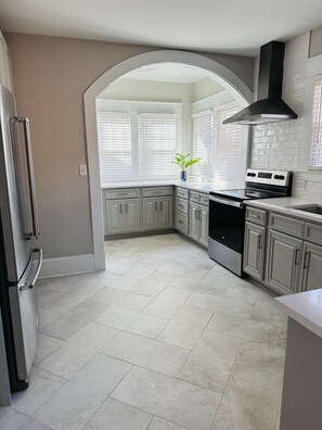 A modern kitchen with white cabinets, a stainless steel refrigerator, and a black range hood. - Beautiful Remodeled Home Located Near Guilford College in Greensboro, NC (Greensboro)