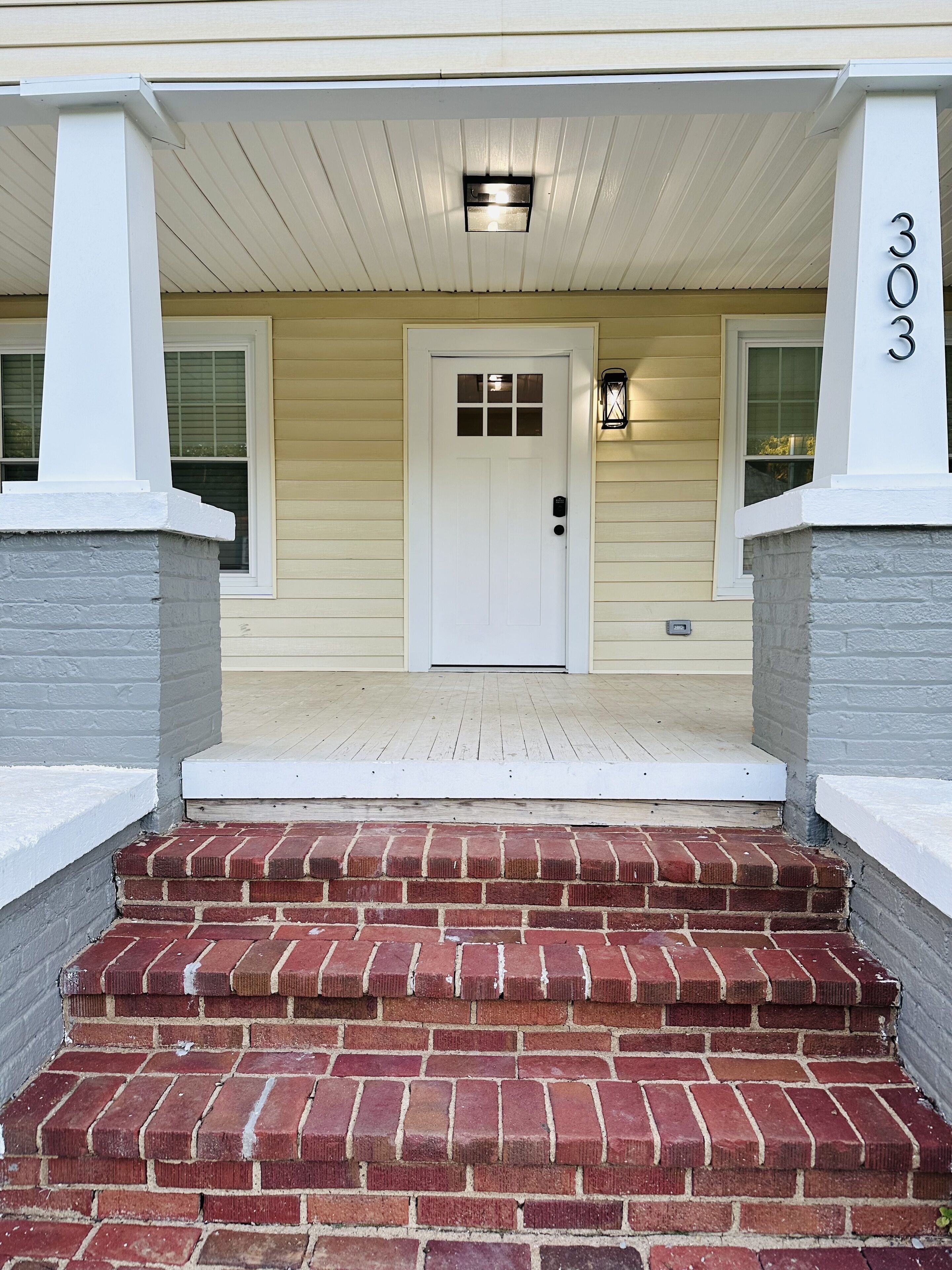 A front entrance with a white door, brick steps, and a number '303' on the wall.