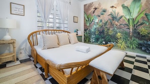 Una habitación con cama, un banco, un mural en la pared, una ventana con cortinas y un suelo a cuadros.