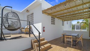 Un patio moderno al aire libre con una mesa y sillas de madera, un sillón colgante y una escalera que lleva a un nivel superior.
