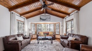 A spacious living room with a high wooden ceiling, two leather sofas, a coffee table, and large windows with blinds. - NEW! Family Cabin Retreat in Munds Park w/ Cozy Back Patio & Loft (Sedona)