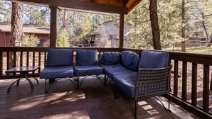 A covered outdoor seating area with a wooden deck, blue cushioned seating, and a glass table. - NEW! Family Cabin Retreat in Munds Park w/ Cozy Back Patio & Loft (Sedona)