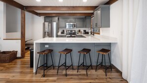 A modern kitchen with a central island, bar stools, and wooden beams on the ceiling. - NEW! Family Cabin Retreat in Munds Park w/ Cozy Back Patio & Loft (Sedona)