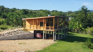 Una cabaña de madera con balcón, rodeada de grava y vegetación.