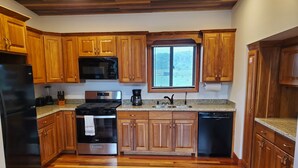 Una cocina con armarios de madera, un refrigerador de acero inoxidable, un microondas, una estufa, un lavavajillas y una ventana con persianas.