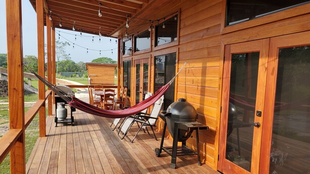 Una terraza de madera con una hamaca, una parrilla y una mesa con sillas.