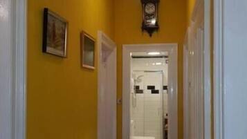 A hallway with yellow walls, a white radiator, a clock, and a door leading to a bathroom.