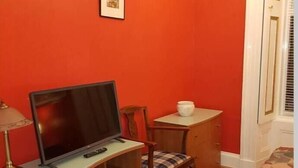 Una habitación pequeña con un escritorio de madera, un televisor, una silla y una mesita con una jarrón blanco.