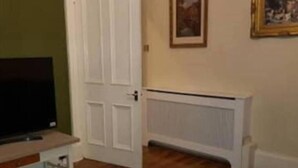 Una sala de estar con televisor, una puerta blanca, un radiador y un cuadro enmarcado en la pared.