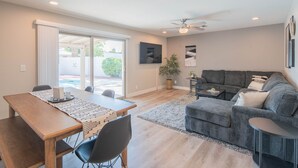 A spacious living area with a wooden dining table, a grey sofa, and a ceiling fan. - Centrally Located Hike Dine & Shop w/ Pool Table, Heated Pool, Office, Firepit (Phoenix)