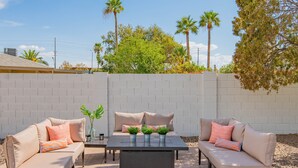 An outdoor patio with a beige sofa set, a table, and potted plants. - Centrally Located Hike Dine & Shop w/ Pool Table, Heated Pool, Office, Firepit (Phoenix)