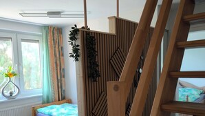 Ein Zimmer mit Bett, Fenster, Heizkörper, einer Holzwand und einer Treppe.