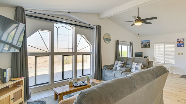 Uma sala de estar espaçosa com uma janela grande, um ventilador de teto e uma TV de tela plana sobre um armário de madeira.