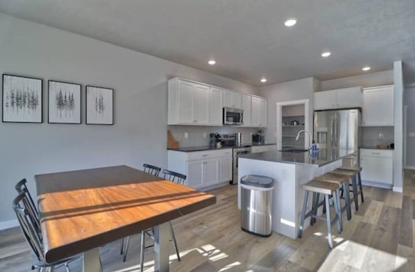 A modern kitchen with white cabinets, a central island, stainless steel appliances, and a dining area with a wooden table and chairs.