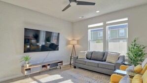 Una sala de estar moderna con un televisor de pantalla plana, un sofá gris, un sillón amarillo y una lámpara de pie.