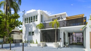 Una casa moderna de dos pisos con balcón, ventanas amplias y plantas en macetas.