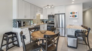 Una cocina moderna con armarios blancos, una mesa de comedor de madera y un refrigerador de acero inoxidable.