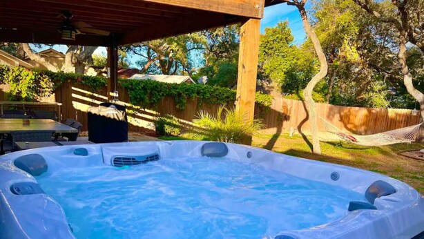 A hot tub under a wooden pergola in a backyard with a wooden fence and trees. - Hot Tub-Dog & Kid Friendly-FREE digital guidebook! (Rockport)