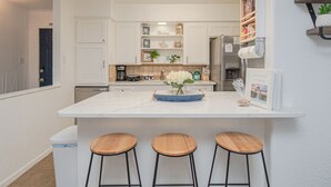 A modern kitchen with white cabinetry, a central island with stools, and a welcome sign. - Hot Tub-Dog & Kid Friendly-FREE digital guidebook! (Rockport)