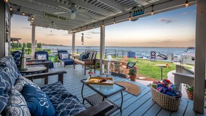 A covered outdoor seating area with a view of the water, furnished with sofas, chairs, and a table with a tray of snacks and drinks. - Karaoke,Arcade,Firepit,PrivateDock,Projector,Kayaks,SUP,Fishing,Massage,Mixology (Montgomery)