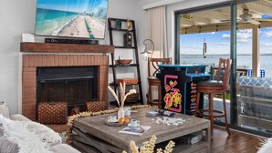 A living room with a fireplace, a large TV, and a view of the sea through a glass door. - Karaoke,Arcade,Firepit,PrivateDock,Projector,Kayaks,SUP,Fishing,Massage,Mixology (Montgomery)