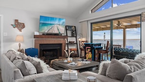 A cozy living room with a fireplace, comfortable seating, a large TV, and a view of the ocean. - Karaoke,Arcade,Firepit,PrivateDock,Projector,Kayaks,SUP,Fishing,Massage,Mixology (Montgomery)